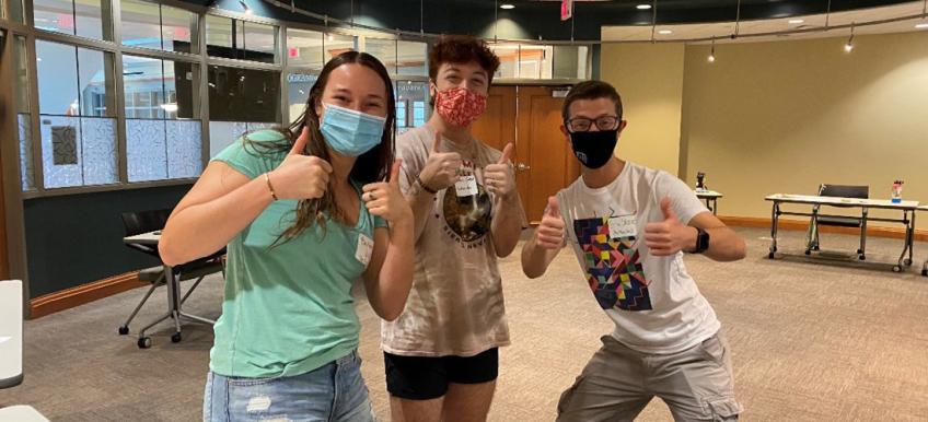 Three students give a thumbs up to the camera