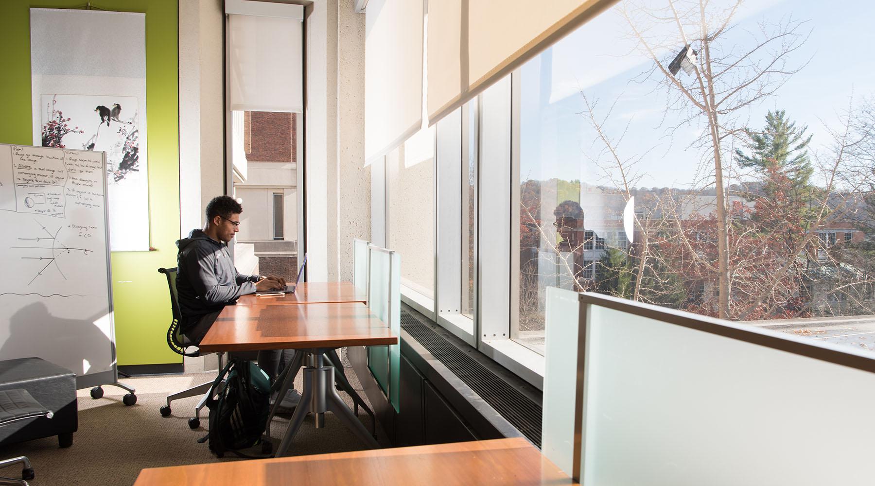 A student works at a laptop in front of a large window