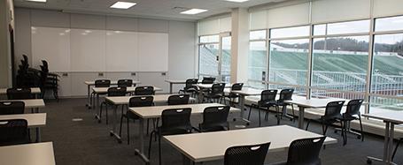Inside a classroom in Sook Center, featuring tables and chairs and a whiteboard at the front of the room