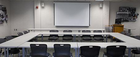 Room inside Sook Center, featuring tables and chairs in an "O" formation, with a whiteboard and podium on one wall