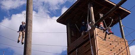 Person standing on a line on a high ropes course, with a climbing wall/building next to them