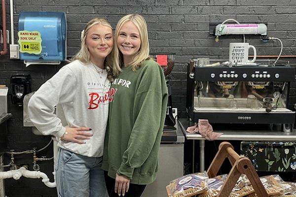 two Coffee Hub employees stand behind the counter smiling in front of the espresso machine