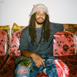 Earl Sweatshirt sitting on red floral couch with plastic covers