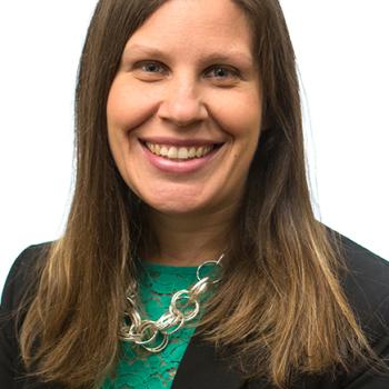 A headshot of Kathy Wilson smiling.  She is wearing a green blouse and black jacket with a necklace.