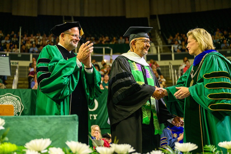 President Lori Stewart Gonzalez shakes hands with David Butcher while Board of Trustees Chair Matthew Evans applauds after Butcher received an honorary degree at Spring Commencement.