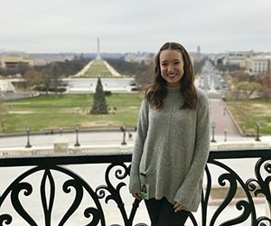 Nicole Dascenzo, who participated in the Scripps Semester in D.C. program during the 2017-18 academic year, is pictured on a balcony in Washington, D.C., with the Washington Monument in the background.