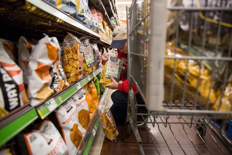 Person kneeling in aisle to stock bags of chips