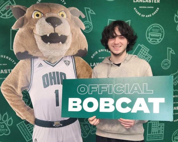 佩顿Wellman holds a sign that says 'Official Bobcat" while he stands next to a cardboard cutout image of Rufus
