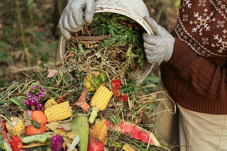 A person pours yard waste into a compost bin.