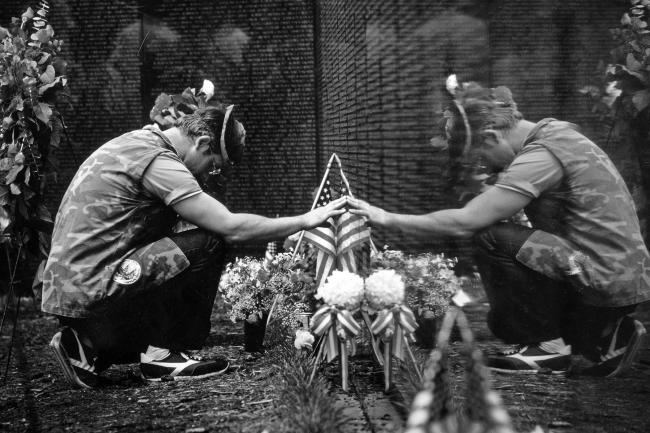 black and white photo of a man kneeling in front of the Vietnam Veterans Memorial