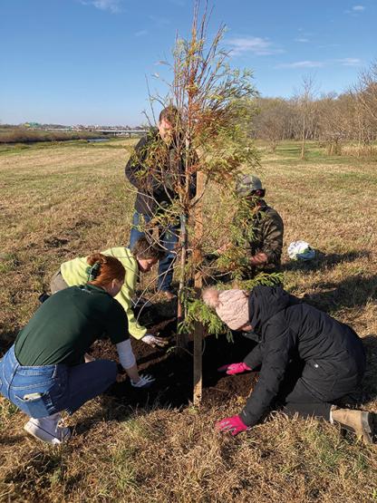 five individuals plant a tree near the Hocking River in late fall or early winter