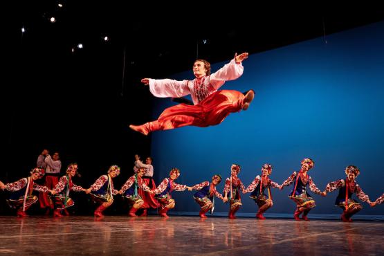 A dancer leaps high into the air while other dancers in colorful costumes dance around him at the 2024 World Music and Dance Concert