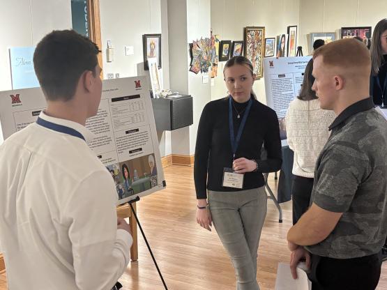 Three individuals discuss a poster presentation at the AURCO conference