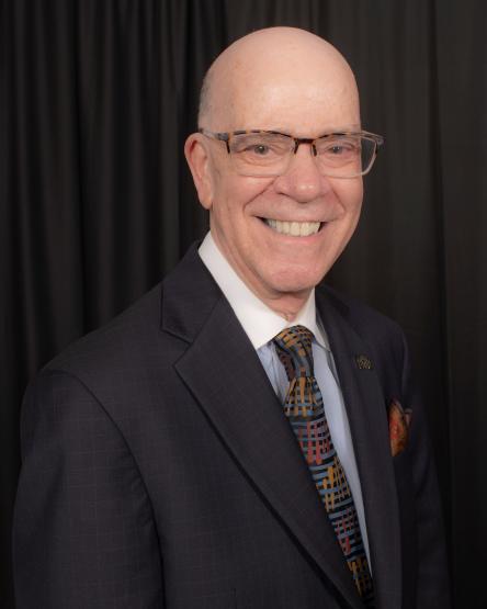 a bald man with glasses and a dark suit, against a black backdrop
