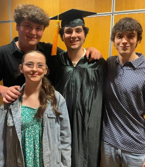 佩顿Wellman is shown wearing his graduation cap and robe while surrounded by family members and friends
