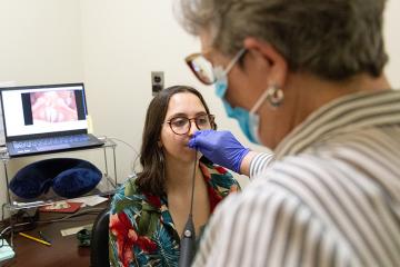 Clinician examines student's vocal chords using a laryngoscope.