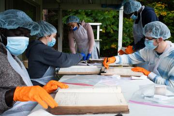 A group of Ohio University students, dressed in masks, gloves and protective hair nets, work to restore historical documents damaged by water and mold.
