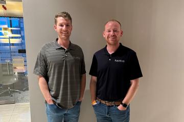 Two men stand side-by-side smiling at the camera
