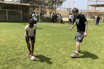 Standing on a baseball field, a man instructs a student who is wearing a blindfold