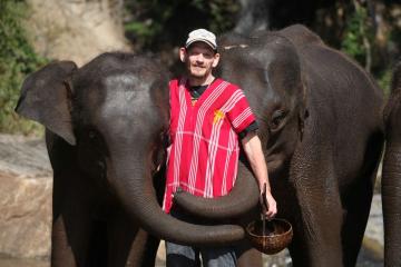 Man in red shirt standing between two elephants