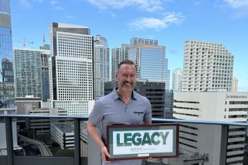 Tim Holt holds the Legacy Award with the backdrop of a city behind him