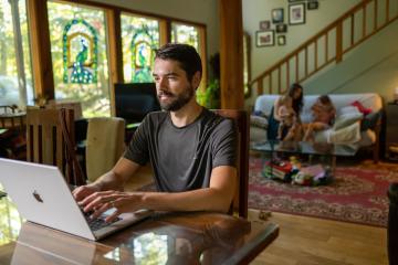 An 威廉希尔亚洲 student is shown working on a computer at home while his family is in the background