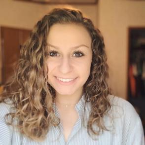 Bailie Ray smiles at the camera, wearing a vertically blue and white striped button-up shirt.