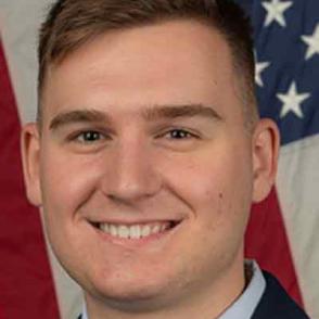 Carter Fee stands in front of an American flag in Air Force uniform, smiling at the camera.