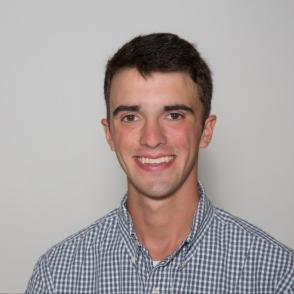 Duncan Farquhar smiles at the camera in front of a white background, wearing a blue and white plaid button-up.