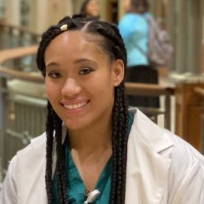 Alexandria Madry smiles at the camera, wearing a white coat over green scrubs.