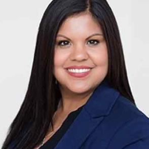 Sylvia Rios smiling at the camera wearing a blue blazer and black shirt.