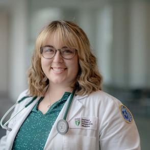 Amy Mehlman Strope wears a green shirt with white dots and a doctor's coat and stethoscope, smiling at the camera
