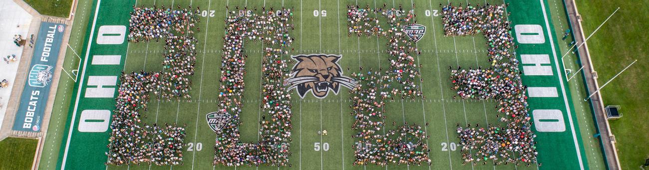 Students stand grouped together on the field of Peden Stadium to spell out 2023.