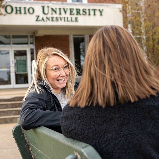 Two students sit on a bench and talk.
