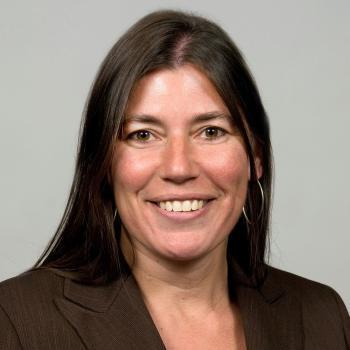 Tracy Plouck headshot. Caucasian woman long brunette hair with dark suit jacket. 