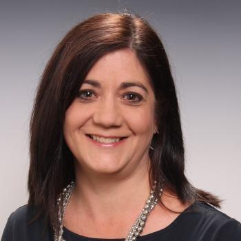 Professional Headshot of a smiling woman with long dark hair, wearing a dark shirt.