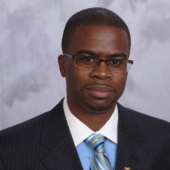 Floun'Say Caver's profile picture Professional headshot of Floun'Say Caver, Black man with glasses wearing a dark suit, blue dress shirt with white color and tie.