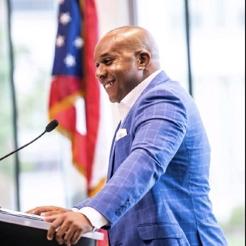 Gary Allen's profile picture Headshot of Gary Allen, African-American man speaking at a podium in a blue suit with white shirt with an American flag in the background