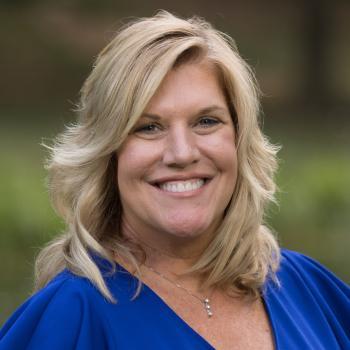 Robin Ambrozy's profile picture Headshot of Robin Ambrozy. A woman smiles at the camera, she has shoulder length blonde hair, and is wearing a royal blue blouse. The background of the image is unfocused landscape.