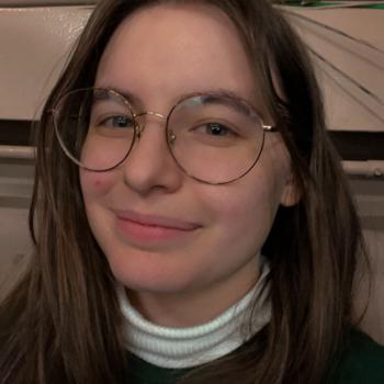 Headshot of Molly Pennington. A woman smiles at the camera, she has brunette hair and is wearing wire framed glasses. 